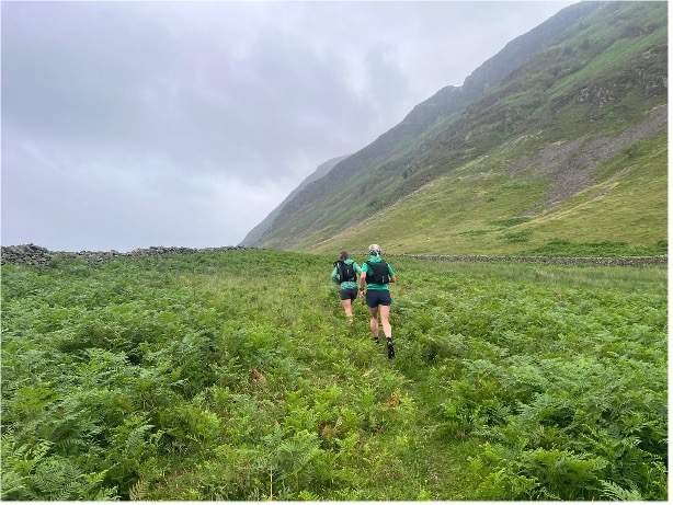Lakes, Meres and Waters report - two women running up away from the camera up a hill through bracken