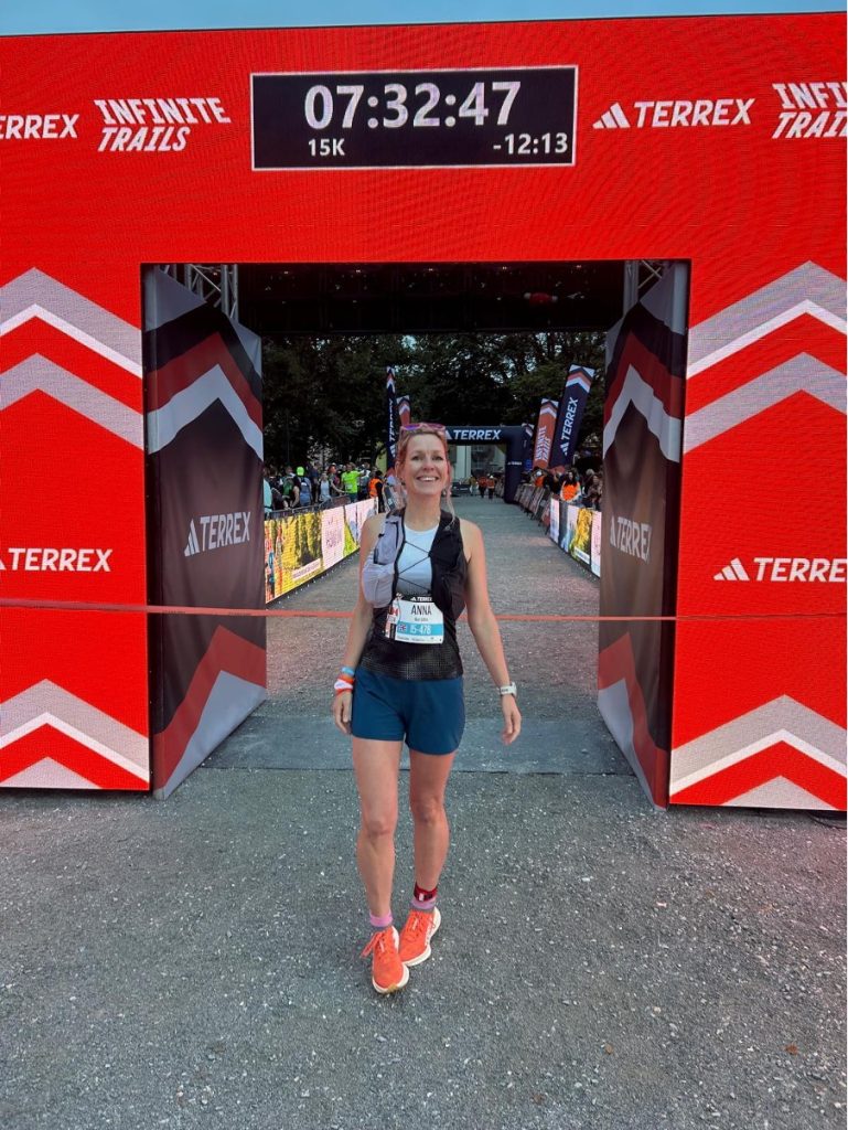 Anna at the finish line of her 15k race with a red finish line gantry behind her. She is smiling and looking happy at the adidas TERREX Infinite Trails in Gastein