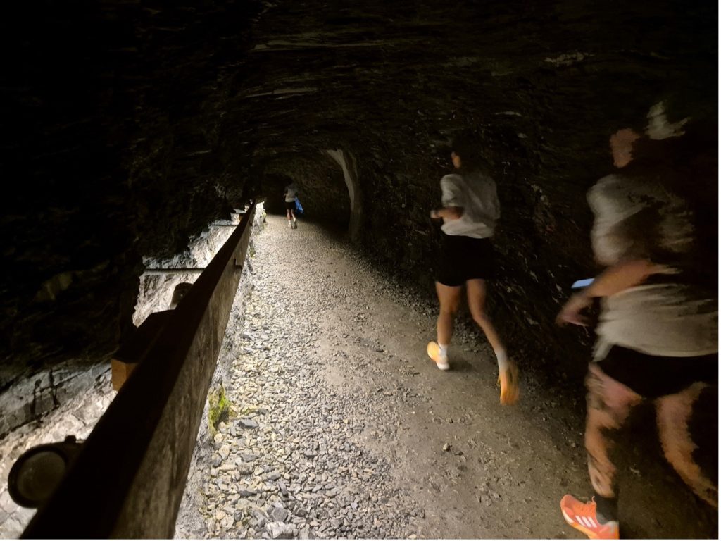 4 runners in white t shirts running along a gravel path in a dark tunnel alongside rushing water at adidas TERREX Infinite Trails in Gastein