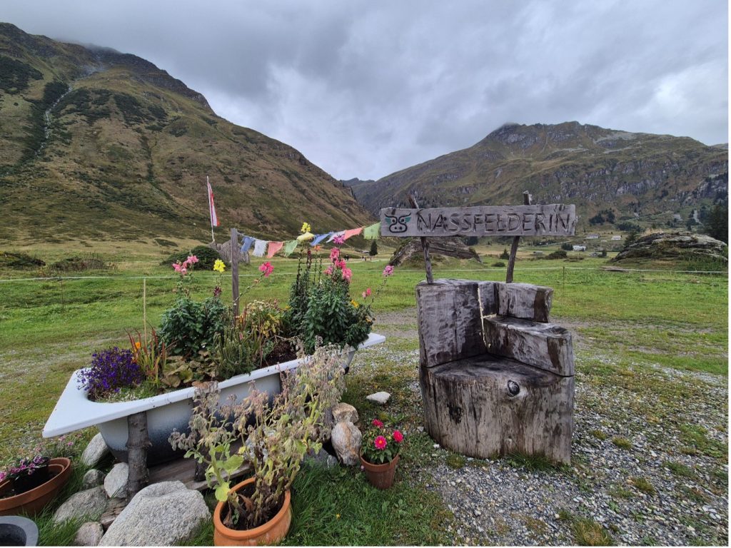 A local scene amidst mountains with a wood carving made out of a tree, a bath filled with flowers and colourful flags at the adidas TERREX Infinite Trails in Gastein