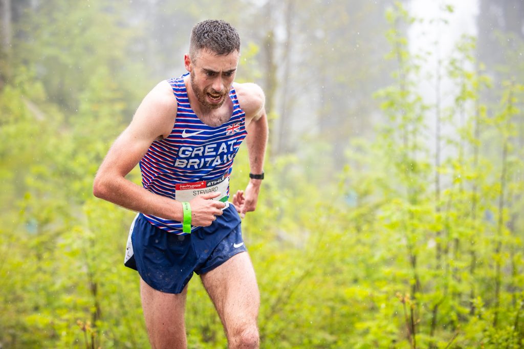 A man in a GB and NI vest running hard up hill