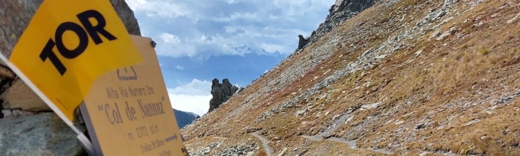 Yellow TOR trail marker and handwritten sign on a rocky alpine slope