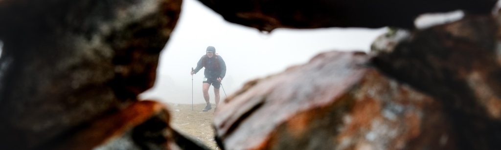 Trail runner moving through mist, viewed through a rocky opening
