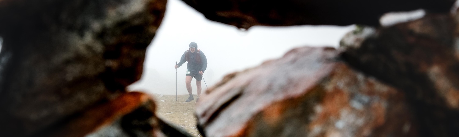Trail runner moving through mist, viewed through a rocky opening