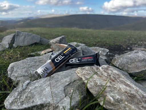 STYRKR CEL50 energy chew packets resting on rocks in a mountain landscape