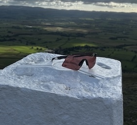 Rudy Project Astral Sphere sunglasses sit on a rock overlooking a cloudy, green Lake District landscape.