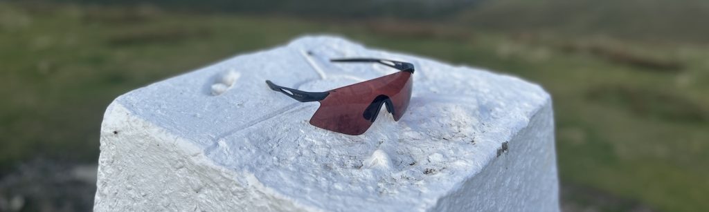 Rudy Project Astral Sphere sunglasses with a reddish lens resting on a pale, textured surface.
