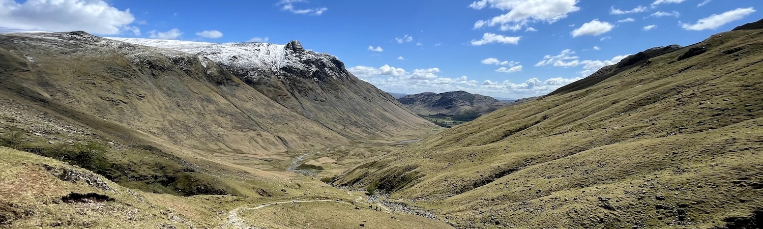 A broad, grassy mountain valley beneath a blue sky with scattered clouds.