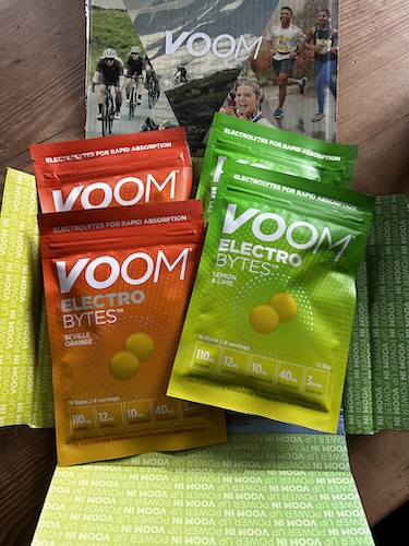Orange and green VOOM Electro Bytes packs overlap a photo of hikers on a mountain trail.
